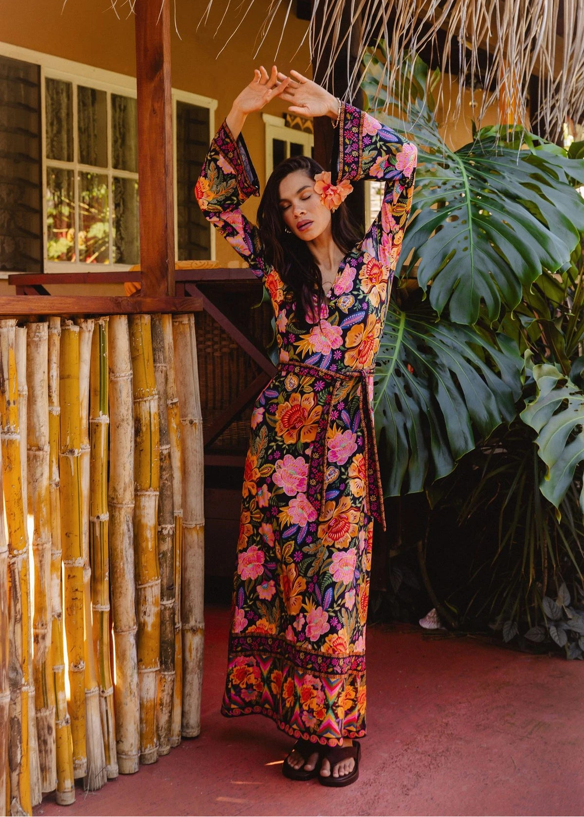 Woman in a colorful floral dress standing on a wooden deck with plants in the background