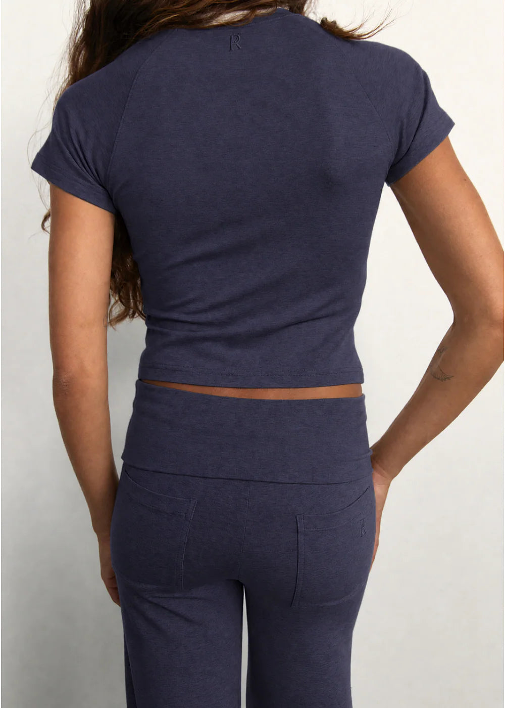 A woman shown from the back wearing a navy blue short-sleeve crop top and matching high-waisted leggings against a light gray background.