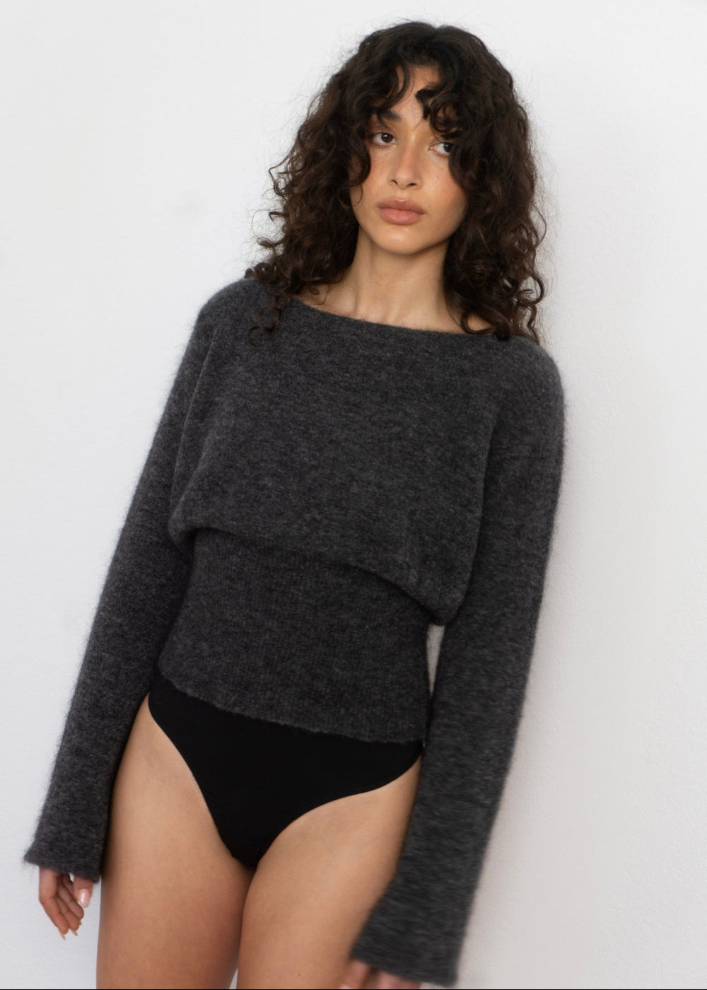 Woman wearing a dark gray sweater over black underwear against a white background