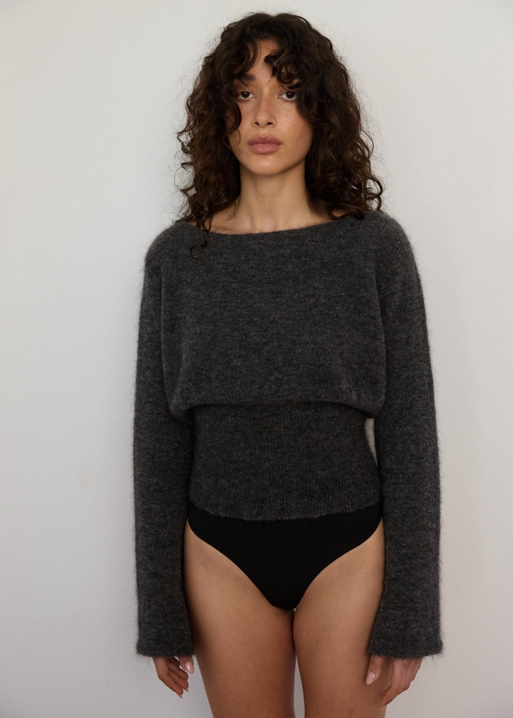 Woman wearing a dark gray sweater over black underwear against a plain background