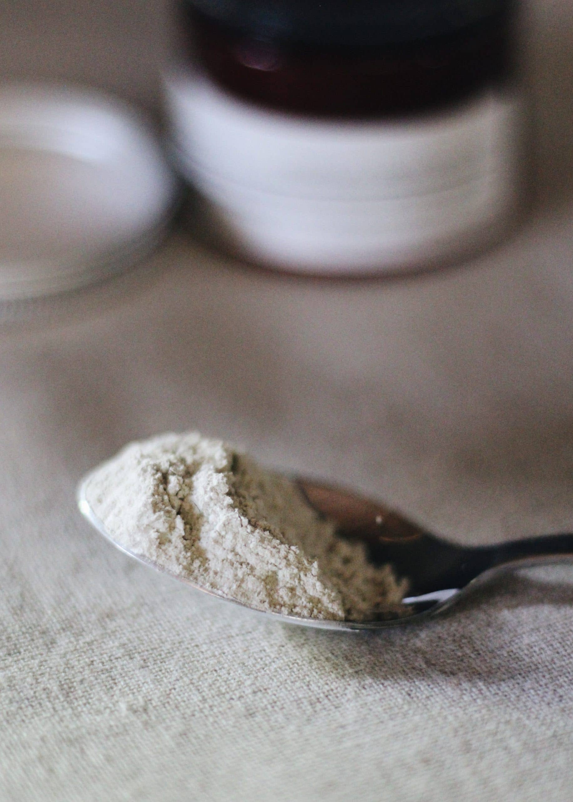 Spoonful of powder on a textured surface with blurred containers in the background