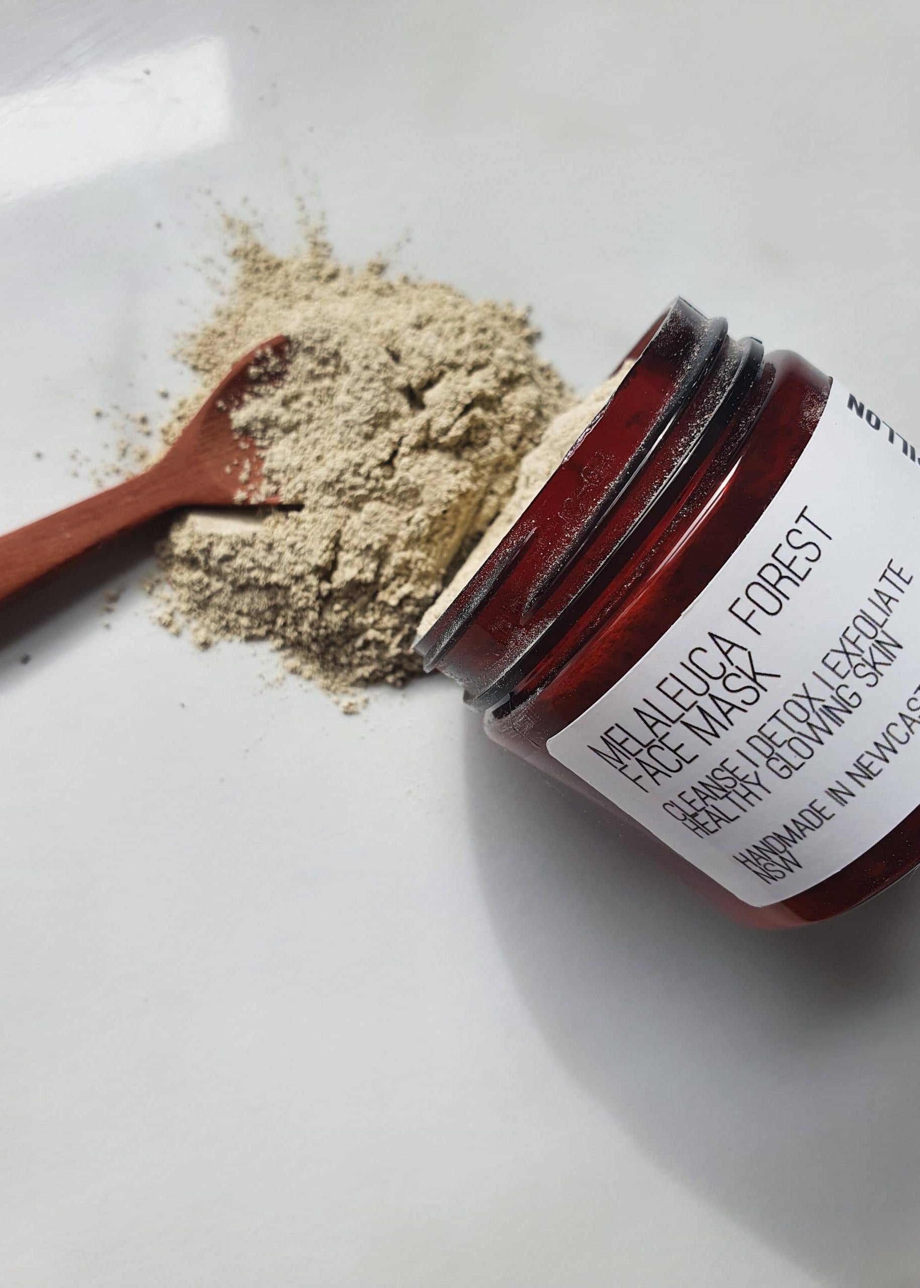 Open jar of face mask with spoonful of powder on a white background