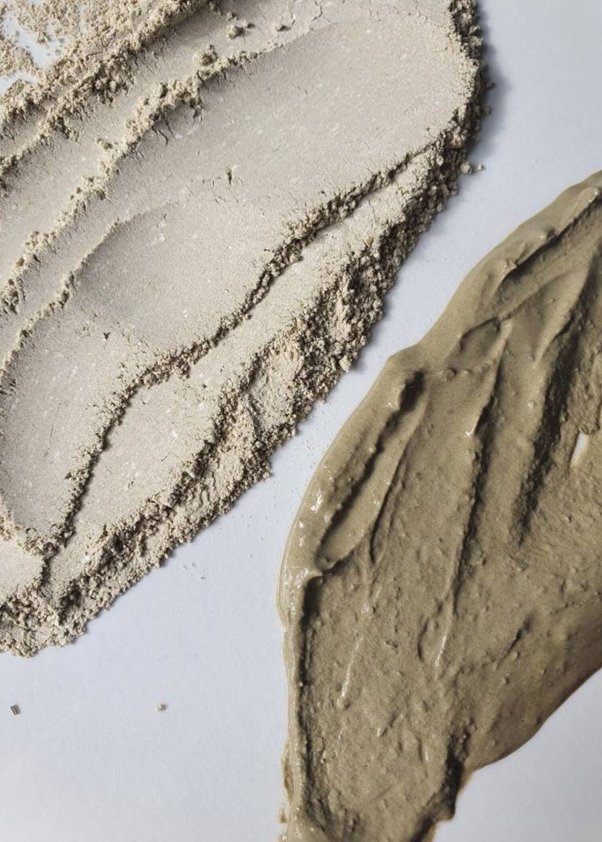 A close-up of a textured cosmetic or clay product swatch, showing a smooth beige powder and a thicker taupe-beige paste on a plain light background.