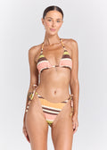 A woman modeling a two-piece string bikini with a retro striped pattern in shades of peach, mustard yellow, brown, and olive green against a light gray studio background.