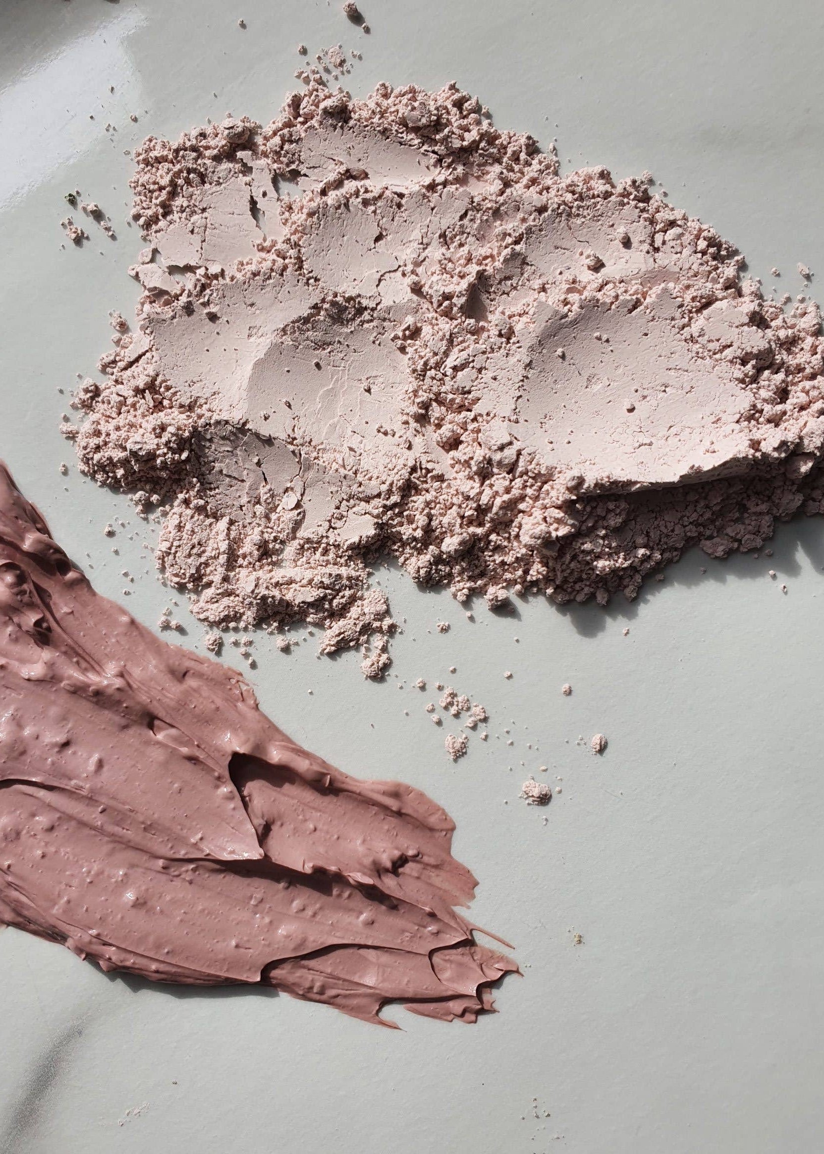 A makeup product shown in two forms: a thick, textured cream swatch and a loose powder, both in a dusty mauve-pink shade on a light gray marble background.