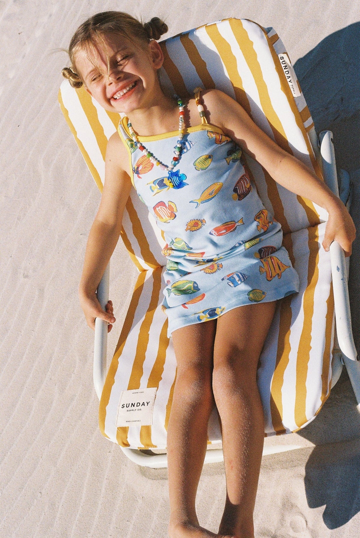 Young girl in a colorful dress sitting on a striped beach chair.