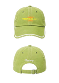 A light green baseball cap shown from the front and back. The front features a yellow and orange 'TROPICAL Spicess' graphic, and the back has 'Stay juicy' embroidered in white script above a silver metal buckle.