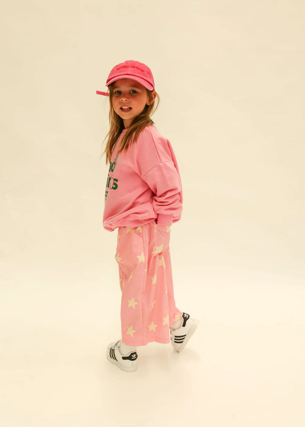 Young girl wearing a pink outfit with a cap on a beige background