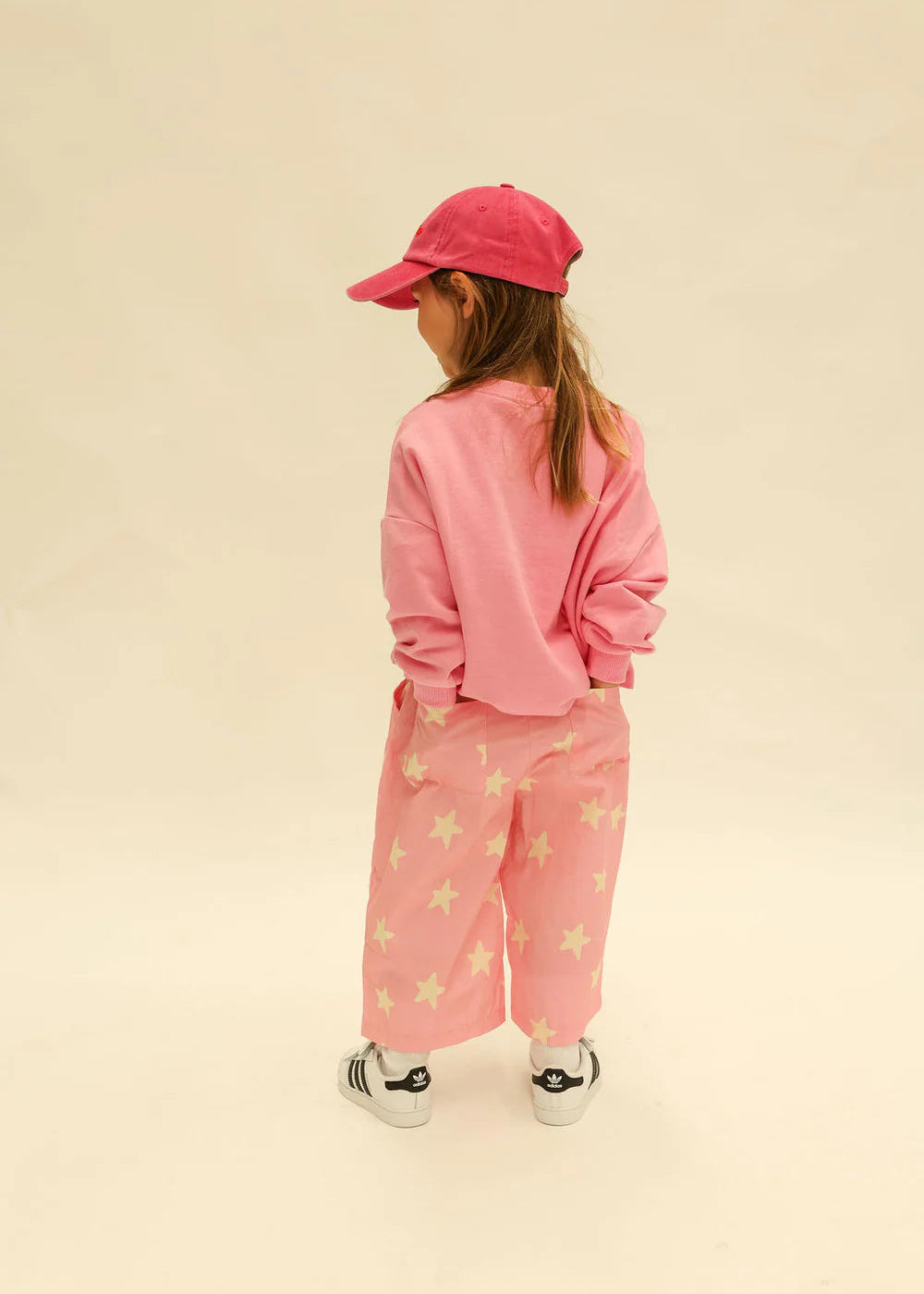 Child wearing a pink outfit with a matching cap on a beige background