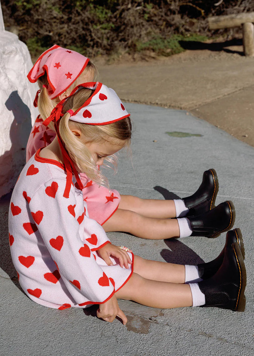 Child wearing a heart-patterned dress and headscarf sitting on a concrete surface.