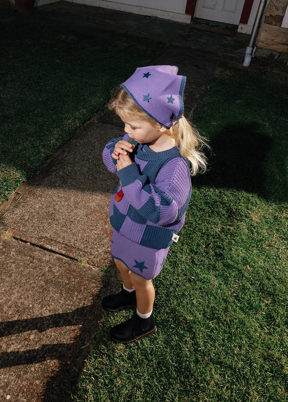 Child in a purple outfit standing on grass outside a house