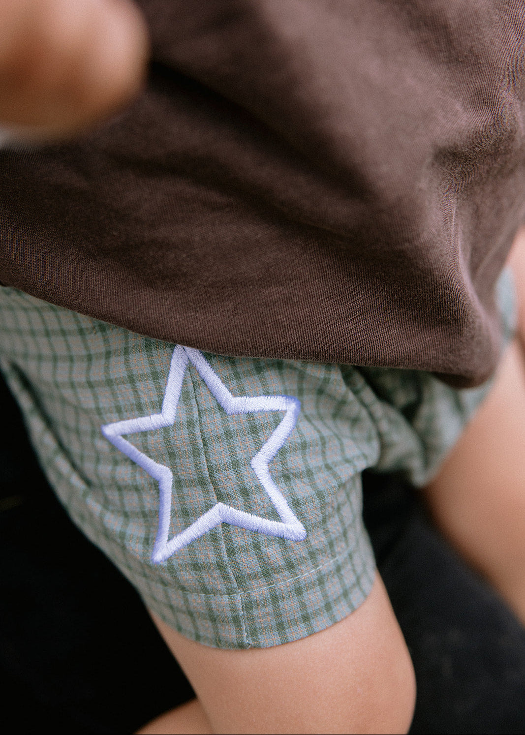 Close-up of a child wearing green and white plaid shorts with a white outlined star applique, paired with a brown shirt.