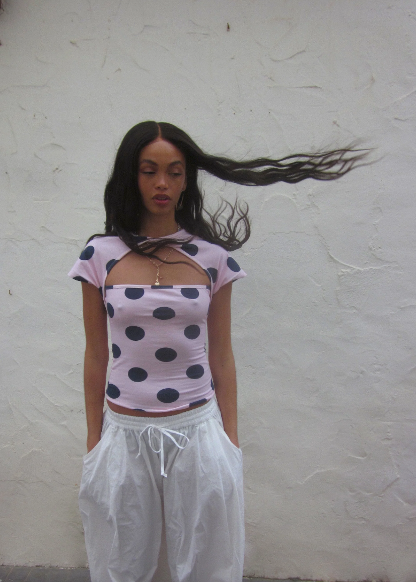 Person wearing a polka dot top and white pants against a plain background