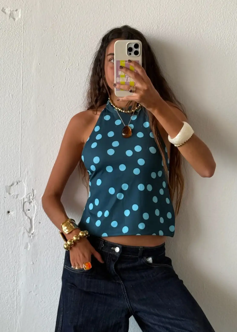 Person wearing a blue polka dot top and dark jeans, taking a mirror selfie.