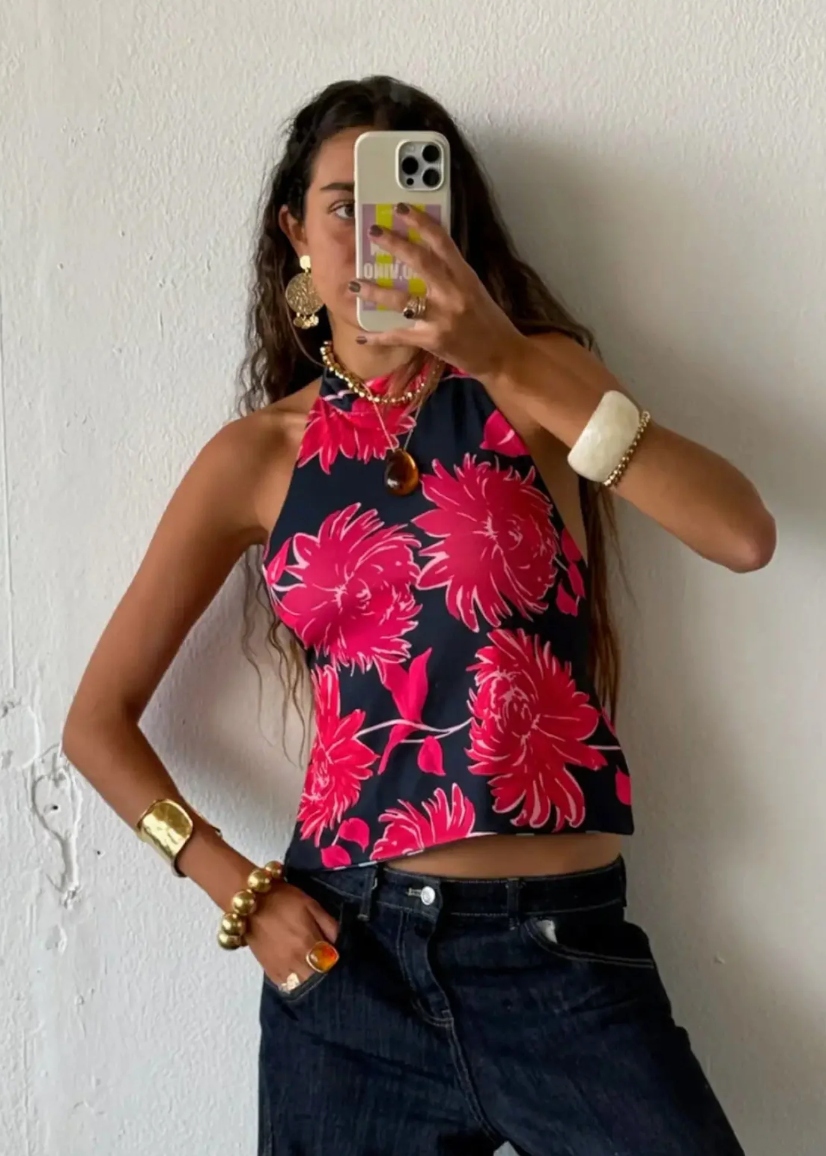 Person wearing a black halter top with pink floral pattern and dark jeans against a white wall.