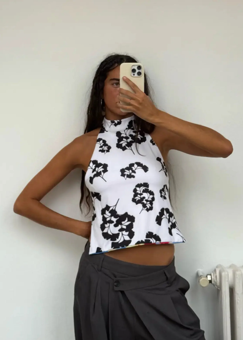 Person wearing a black and white floral top against a plain wall.