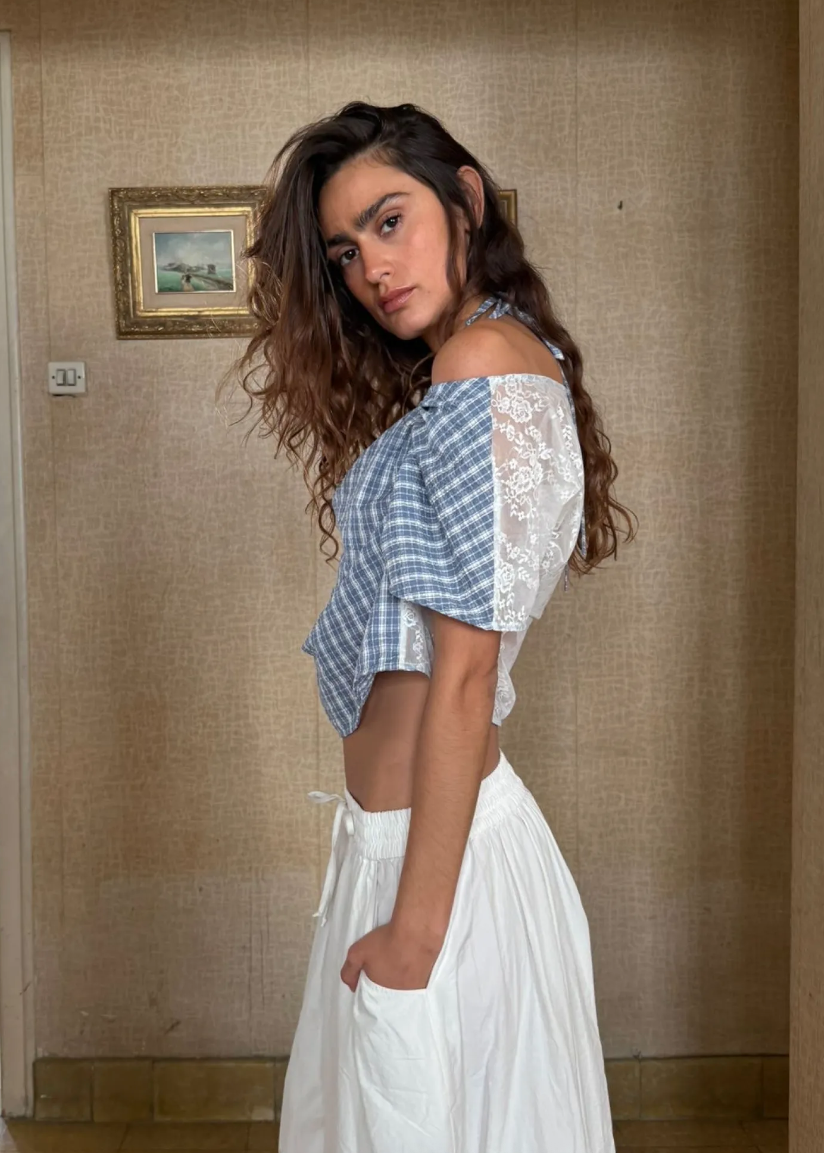 Woman wearing a blue and white top and white skirt in a room with beige walls.