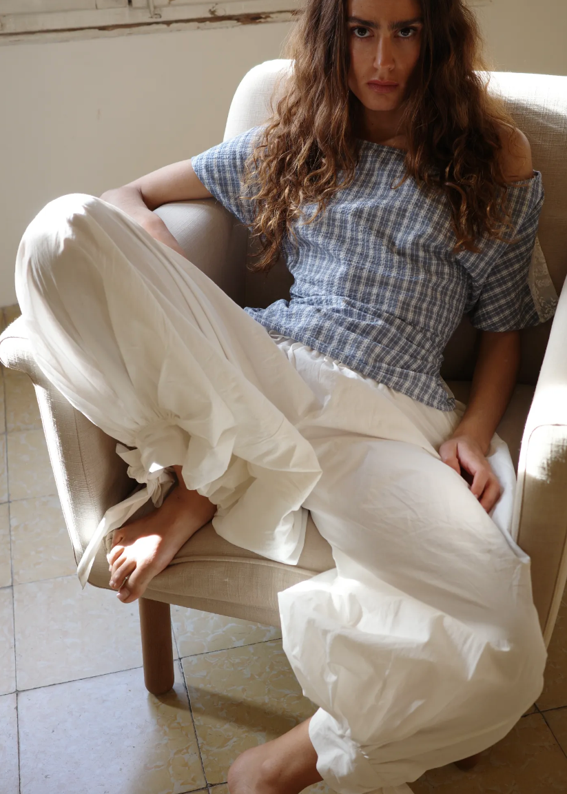 Woman sitting on a chair wearing a checkered top and white pants.