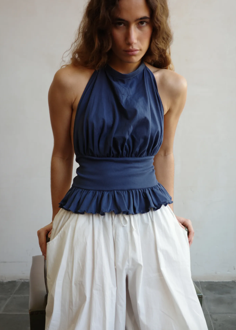 Woman wearing a blue halter top with a peplum waist and white pants against a plain background