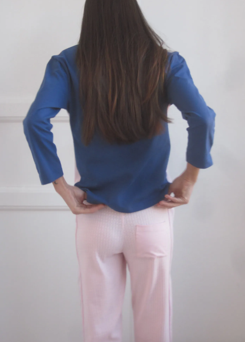 Person wearing a blue top and pink pants with a plain background