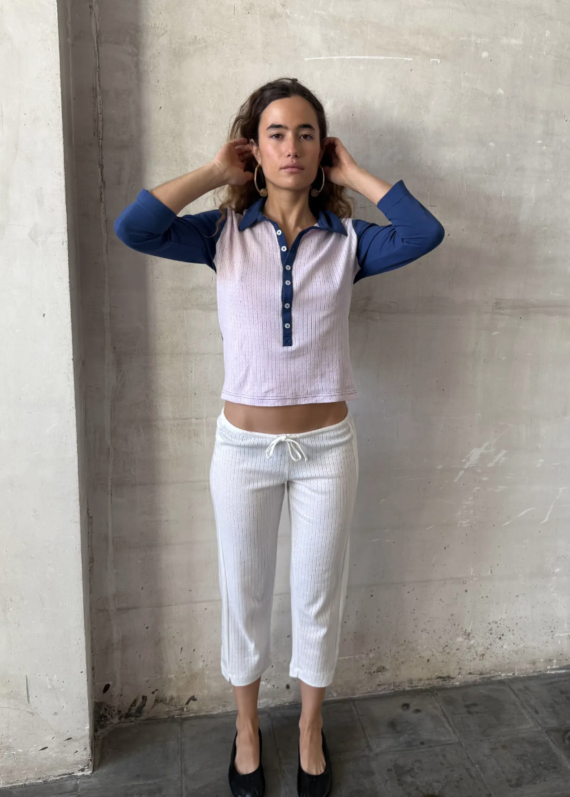 Person wearing a two-tone shirt and white pants against a concrete wall.