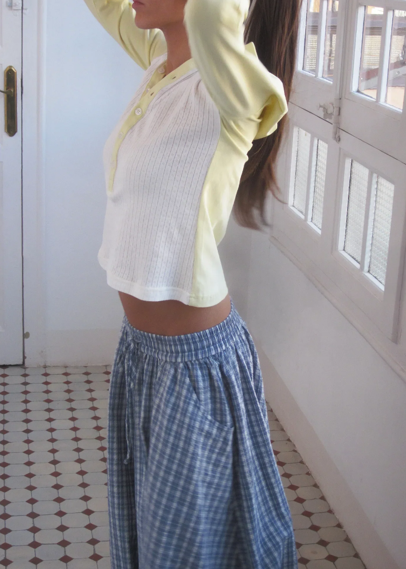 Person wearing a yellow long-sleeve top and blue checkered pants in a room with white walls and a patterned floor.