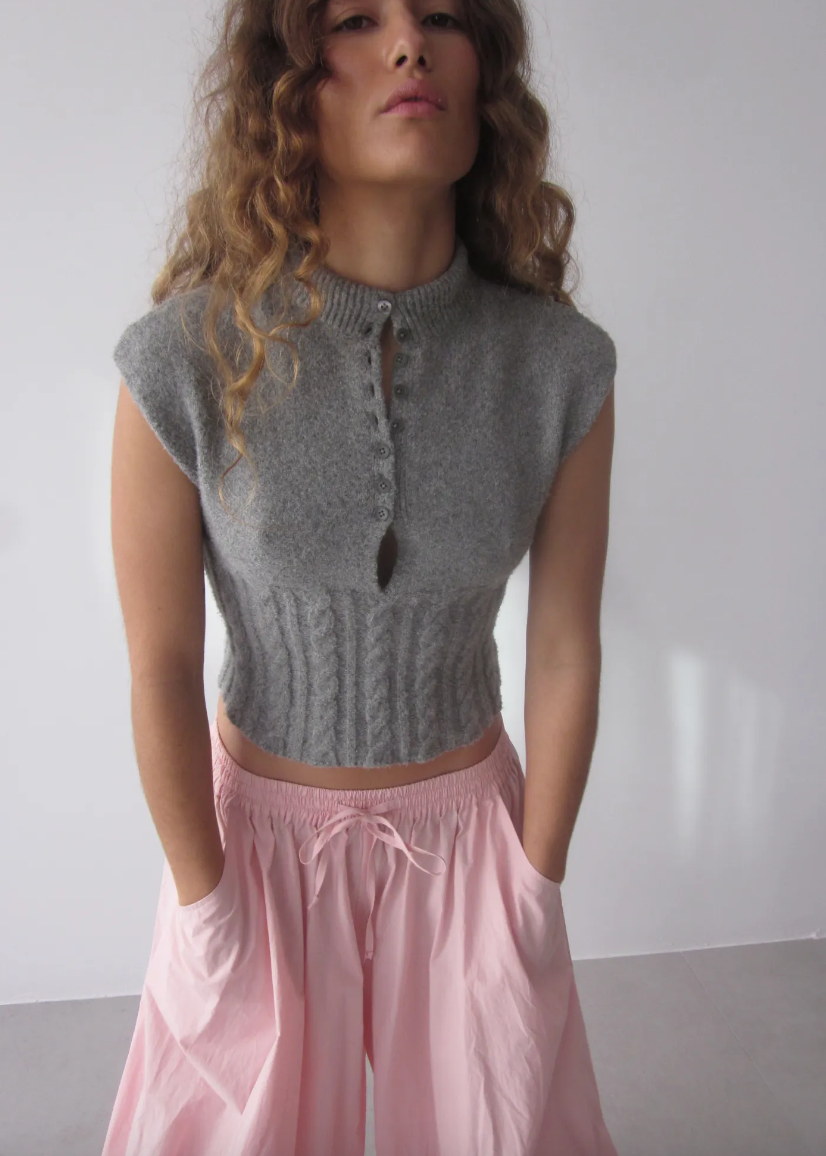 Woman wearing a gray sleeveless knit top and pink pants against a plain background