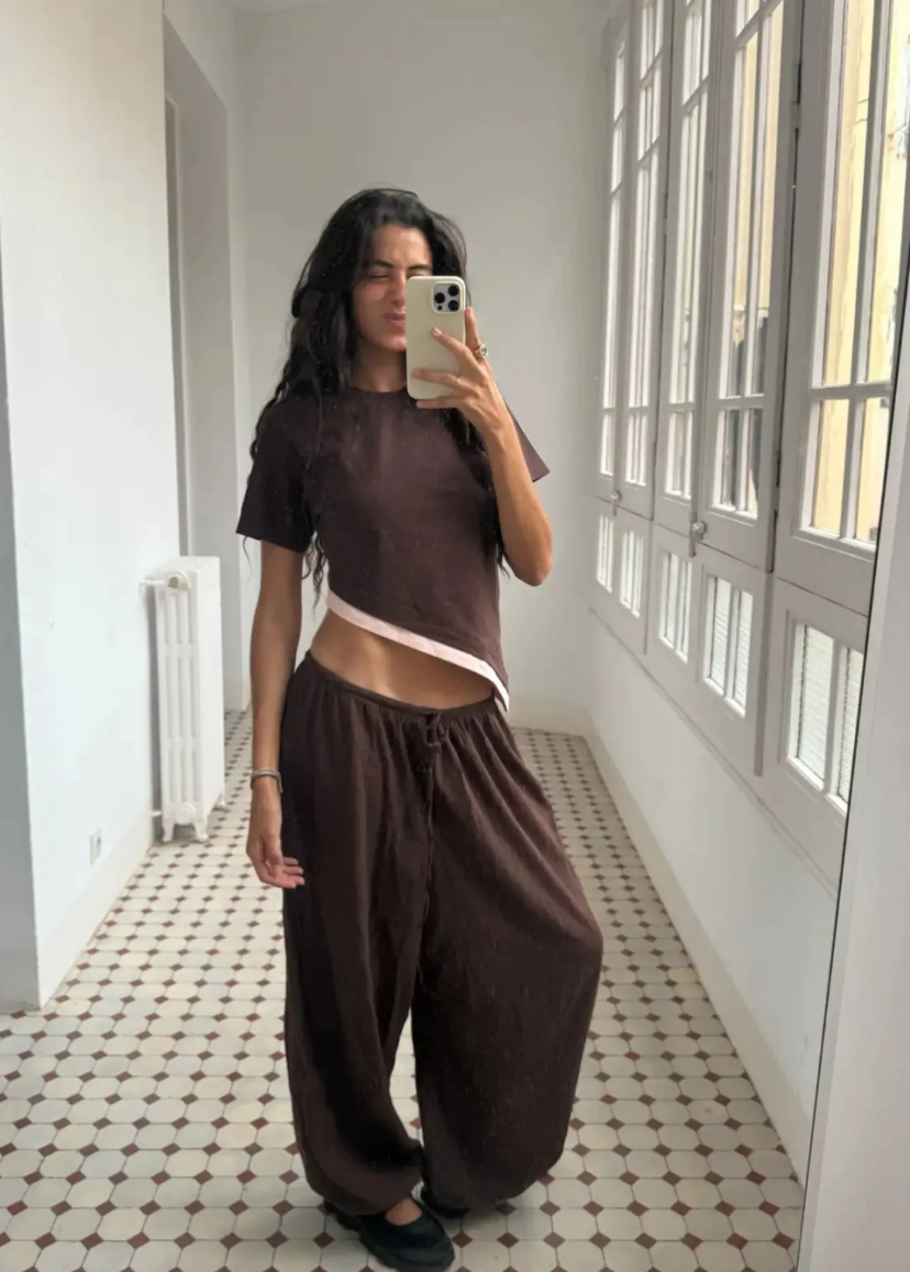 Person taking a mirror selfie wearing a brown outfit in a room with large windows.