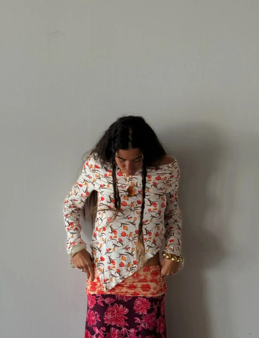 Person wearing a floral blouse and patterned skirt against a plain background