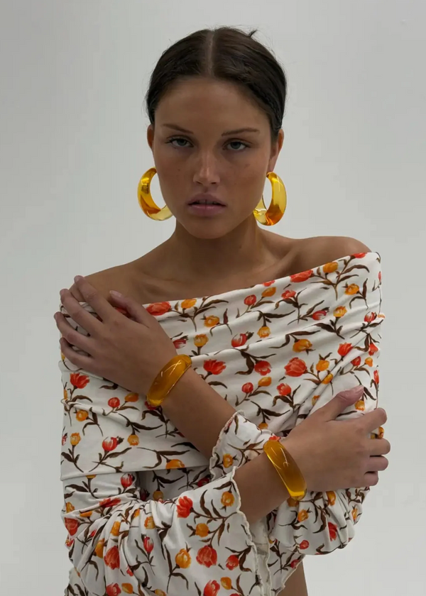 Woman wearing a floral off-shoulder top with yellow accessories on a plain background