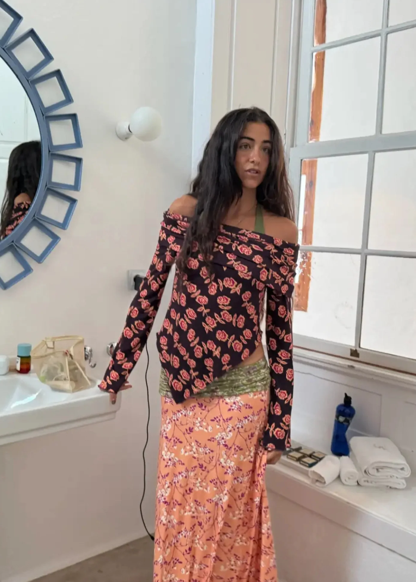 Woman in a floral off-shoulder top and pink skirt standing in a bathroom.