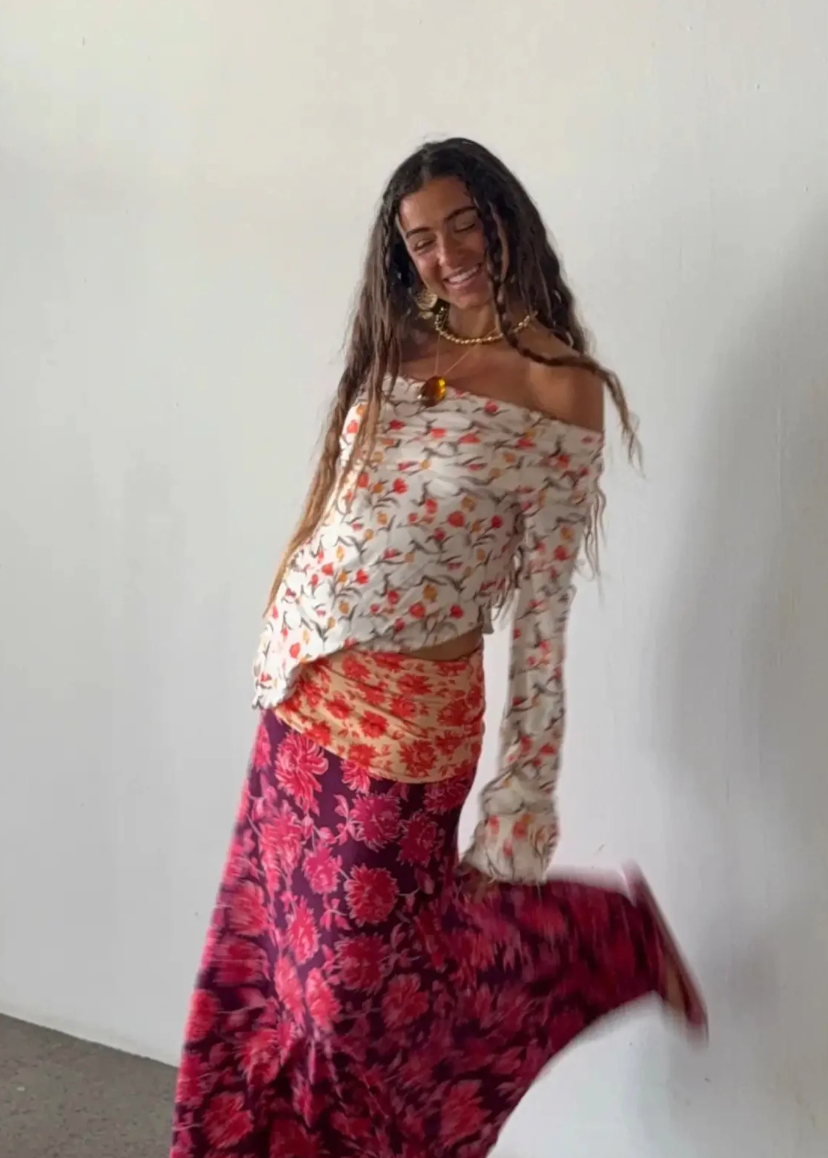 Woman wearing a floral off-shoulder top and a long, patterned skirt against a white background.