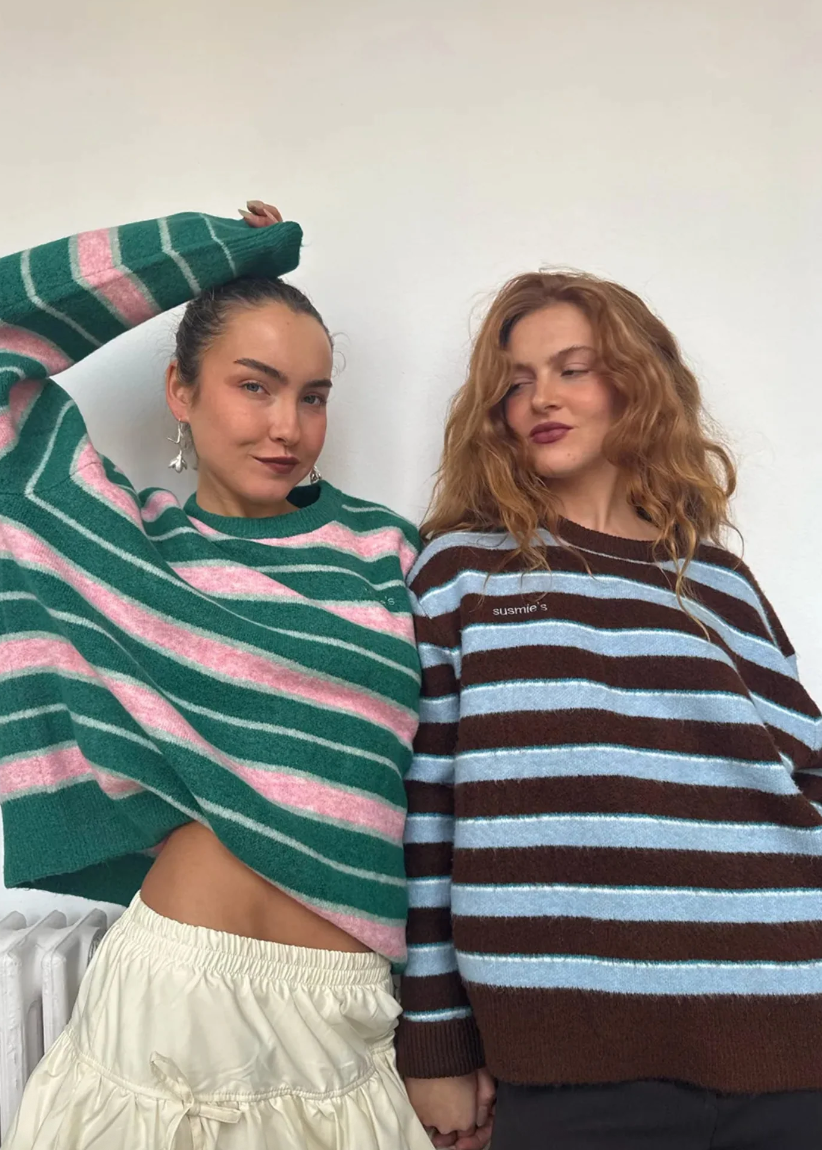Two women wearing colorful striped sweaters against a plain background