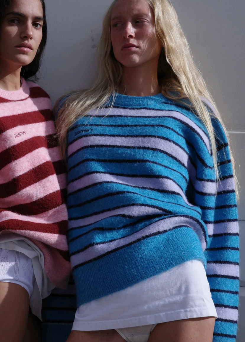 Two women wearing colorful striped sweaters against a plain background