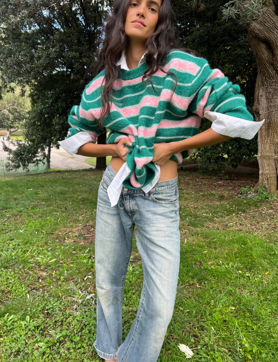Person wearing a green and pink striped sweater with rolled-up sleeves in an outdoor setting.