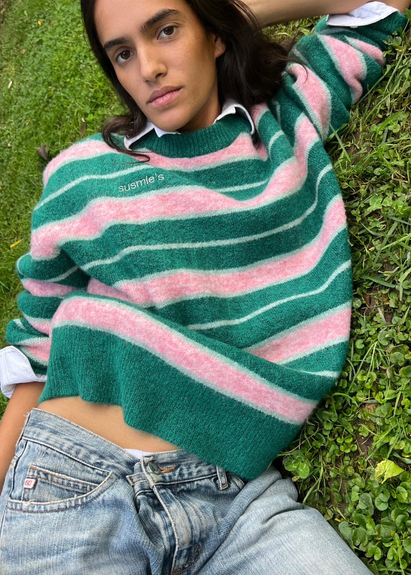 Person wearing a green and pink striped sweater sitting on grass