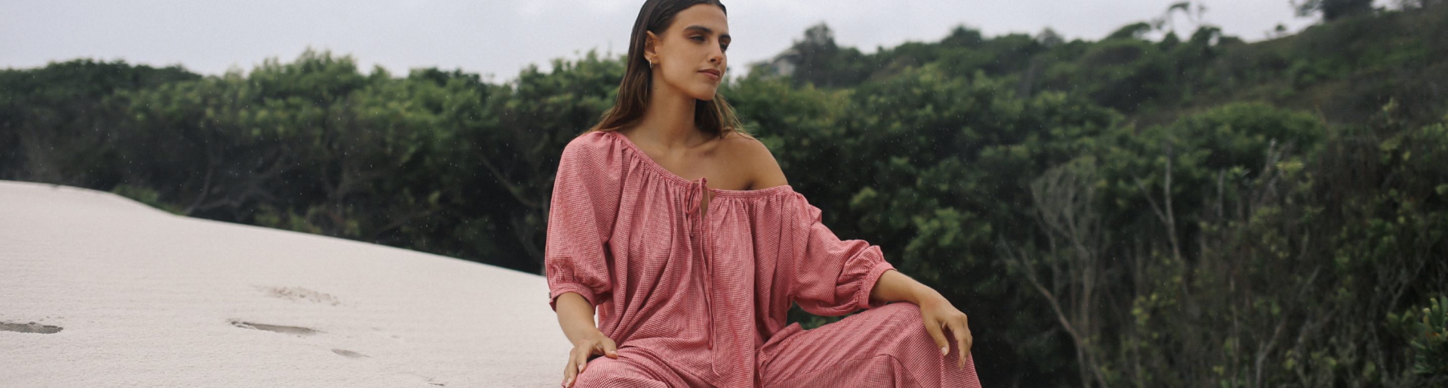 Woman in a pink dress sitting on sand with greenery in the background