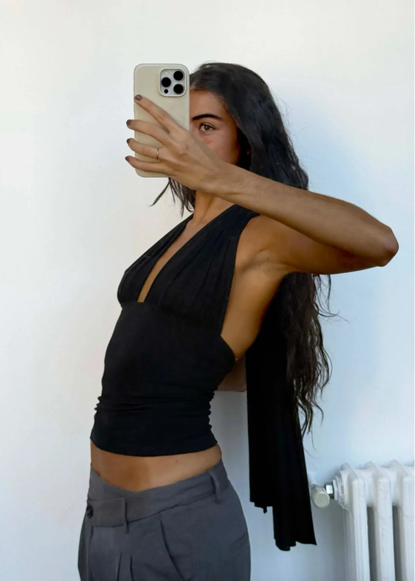 Person wearing a black top and gray pants taking a mirror selfie.