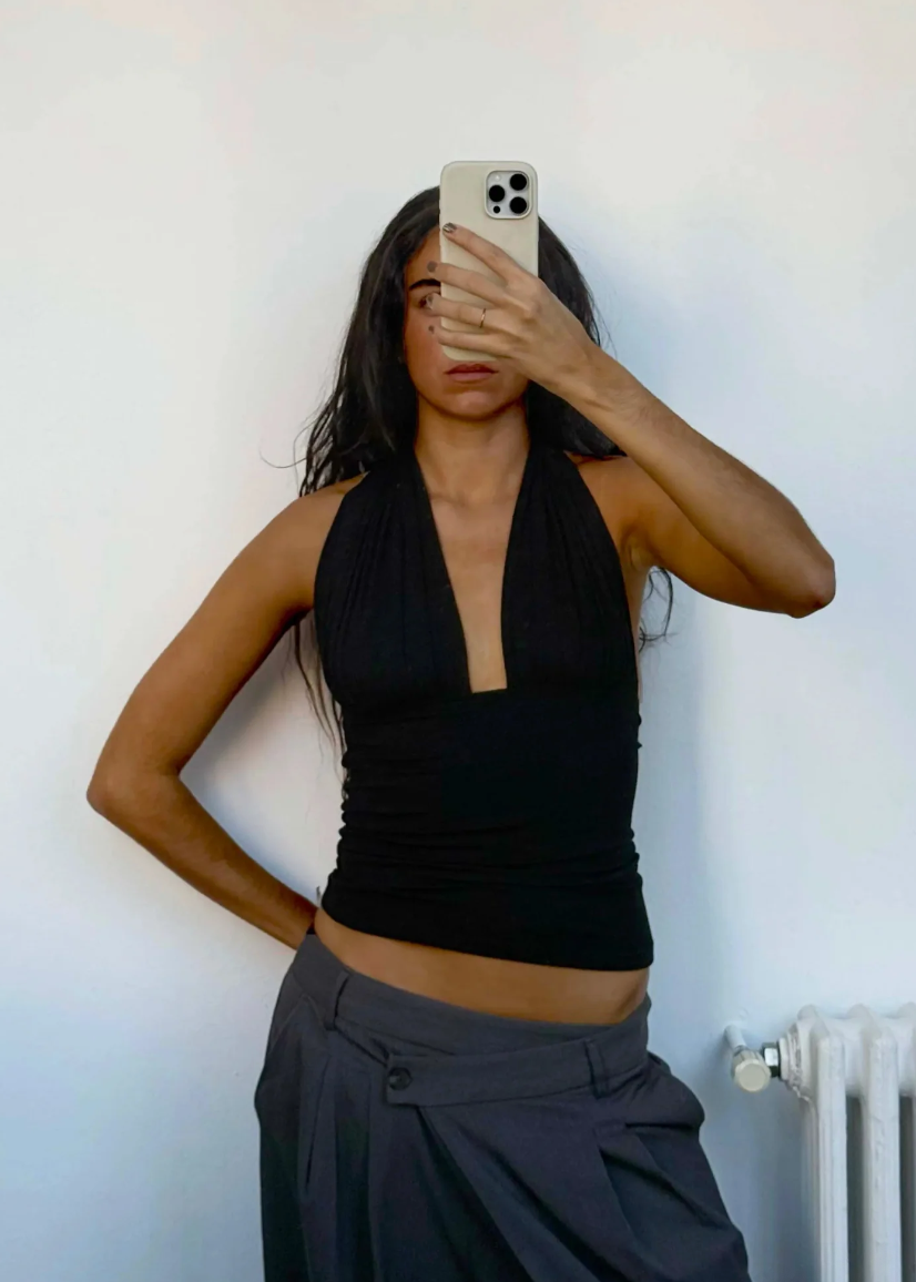 Person wearing a black halter top and gray pants against a white wall.