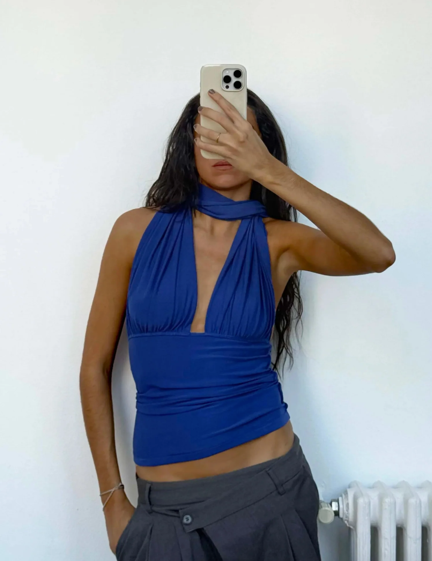 Person wearing a blue halter top and gray pants against a white wall.