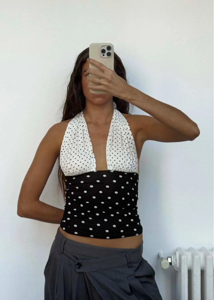 Person wearing a black and white polka dot halter top against a plain background
