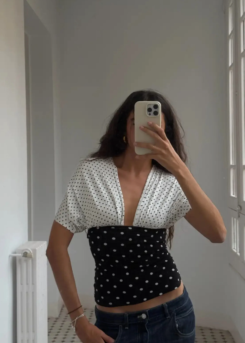 Person wearing a black and white polka dot top in a room with a window.