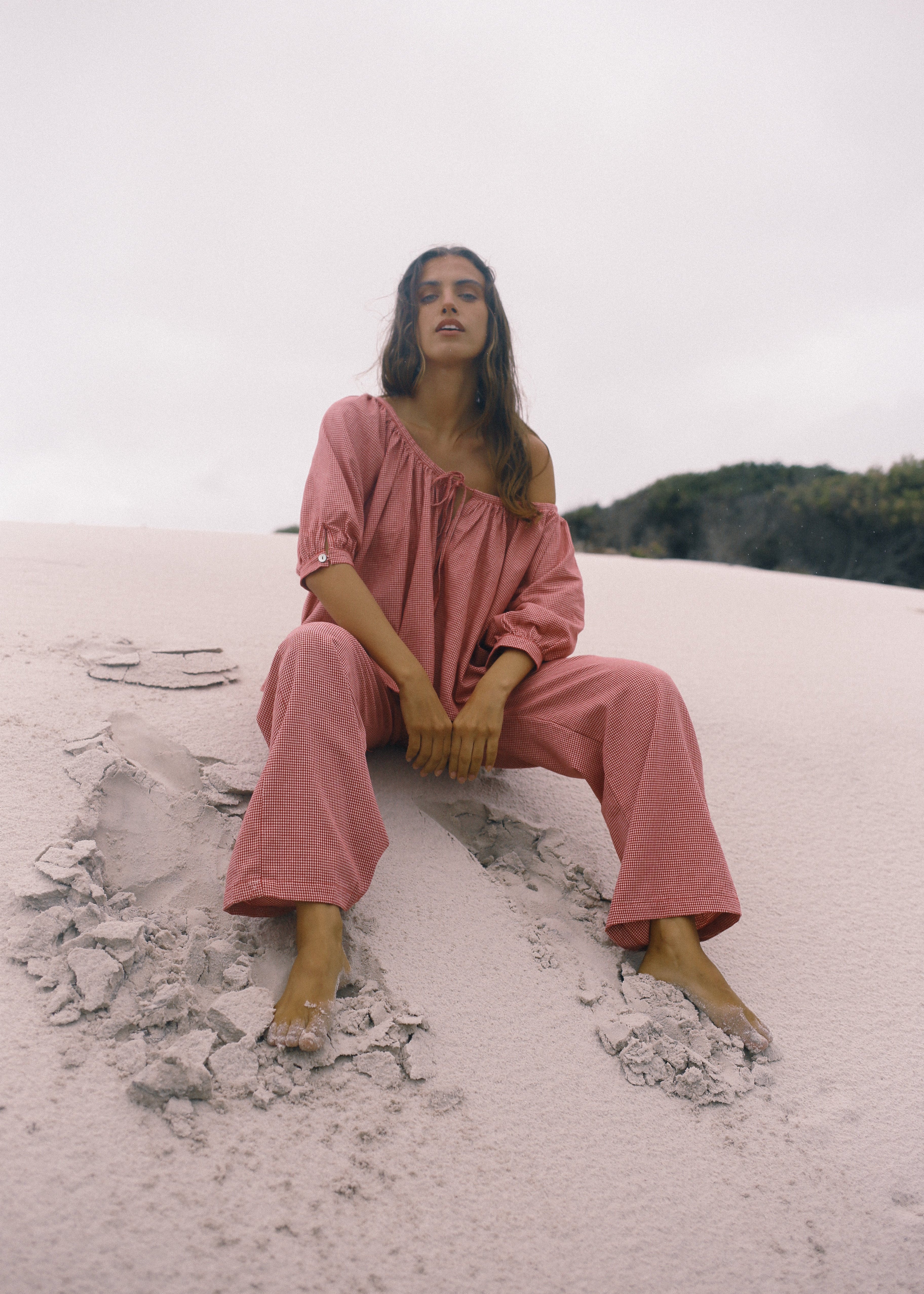 Woman in a pink outfit sitting on a rocky surface with a natural landscape in the background