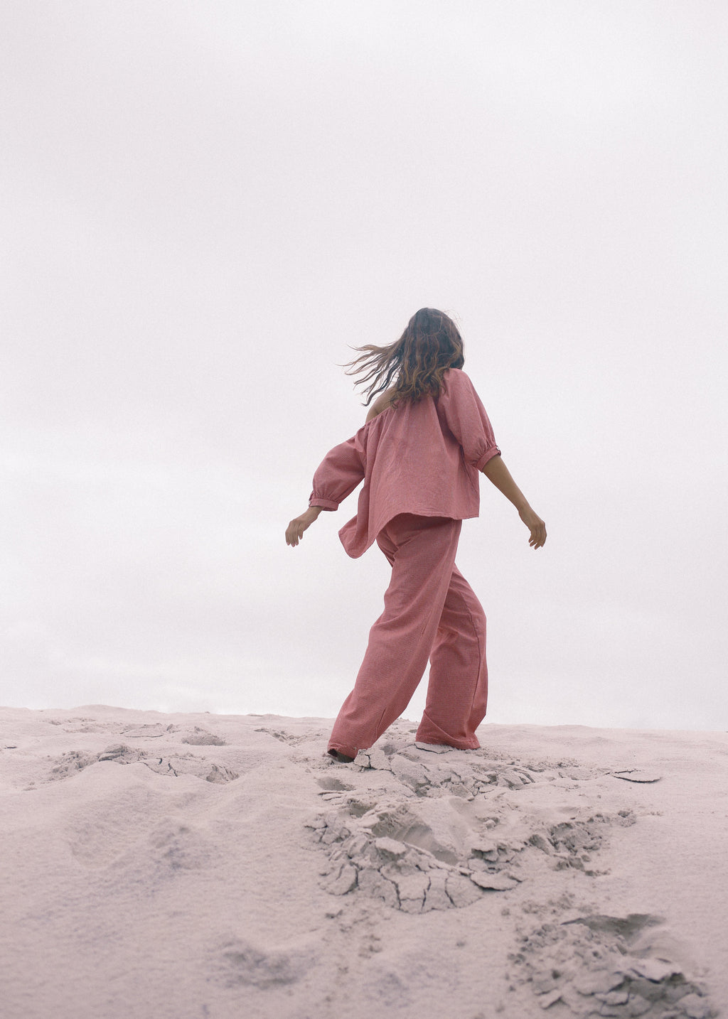 Person in a pink outfit standing on sand with a white background