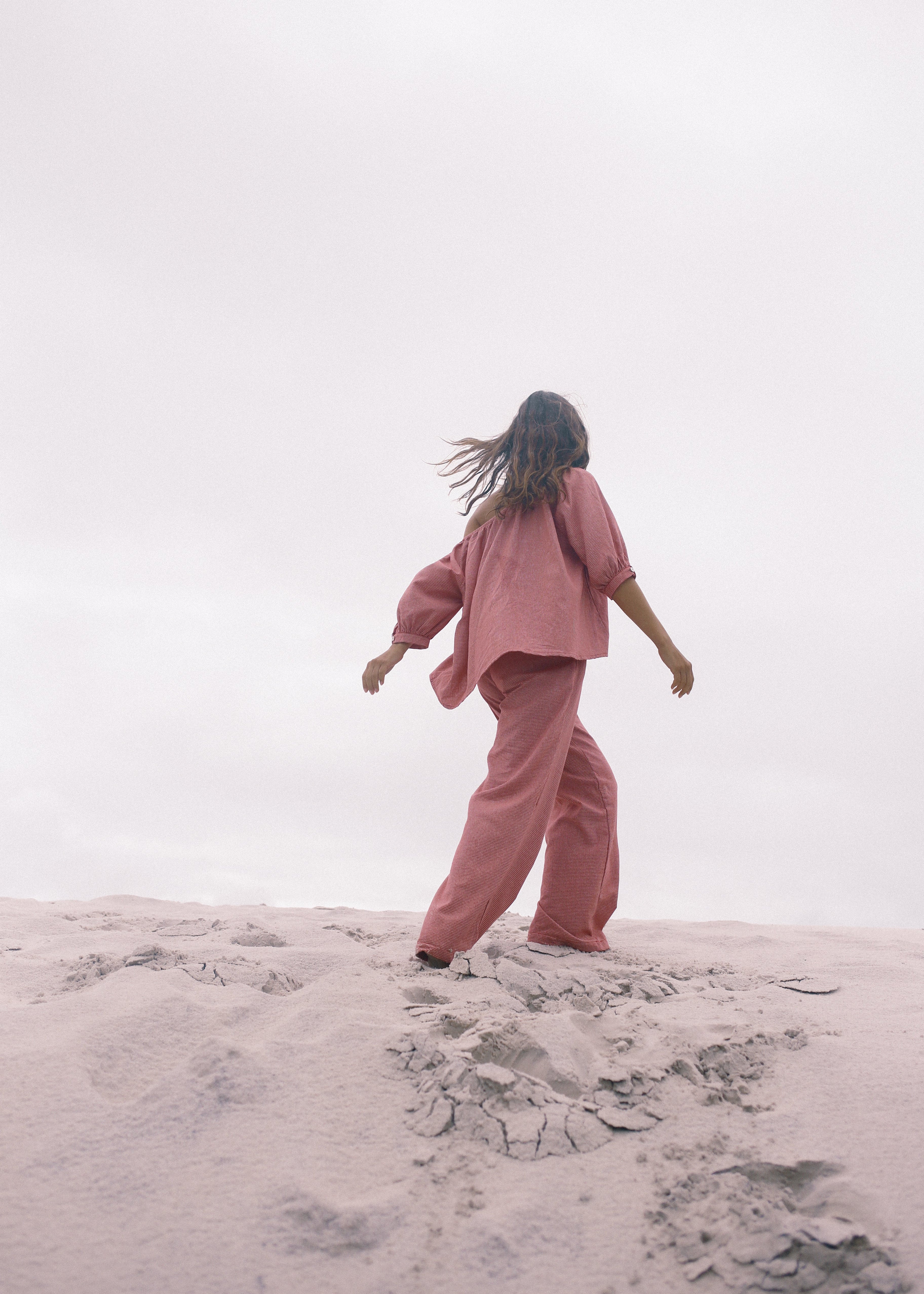 Person in a pink outfit standing on sand with a white background