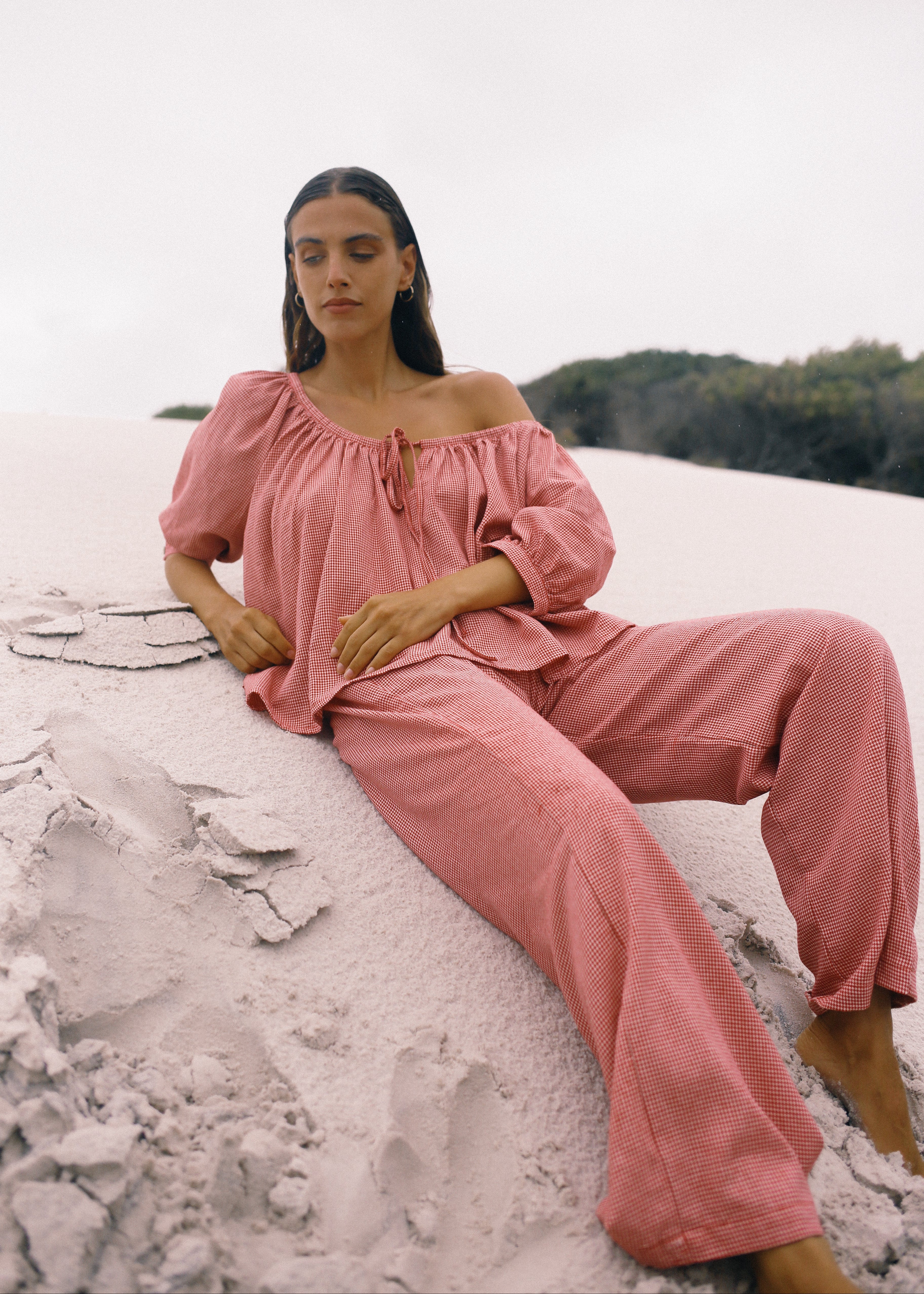 Woman in pink off-shoulder top and pants sitting on a rocky surface with a natural background