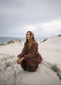 Woman in a brown outfit sitting on a sandy dune with ocean in the background