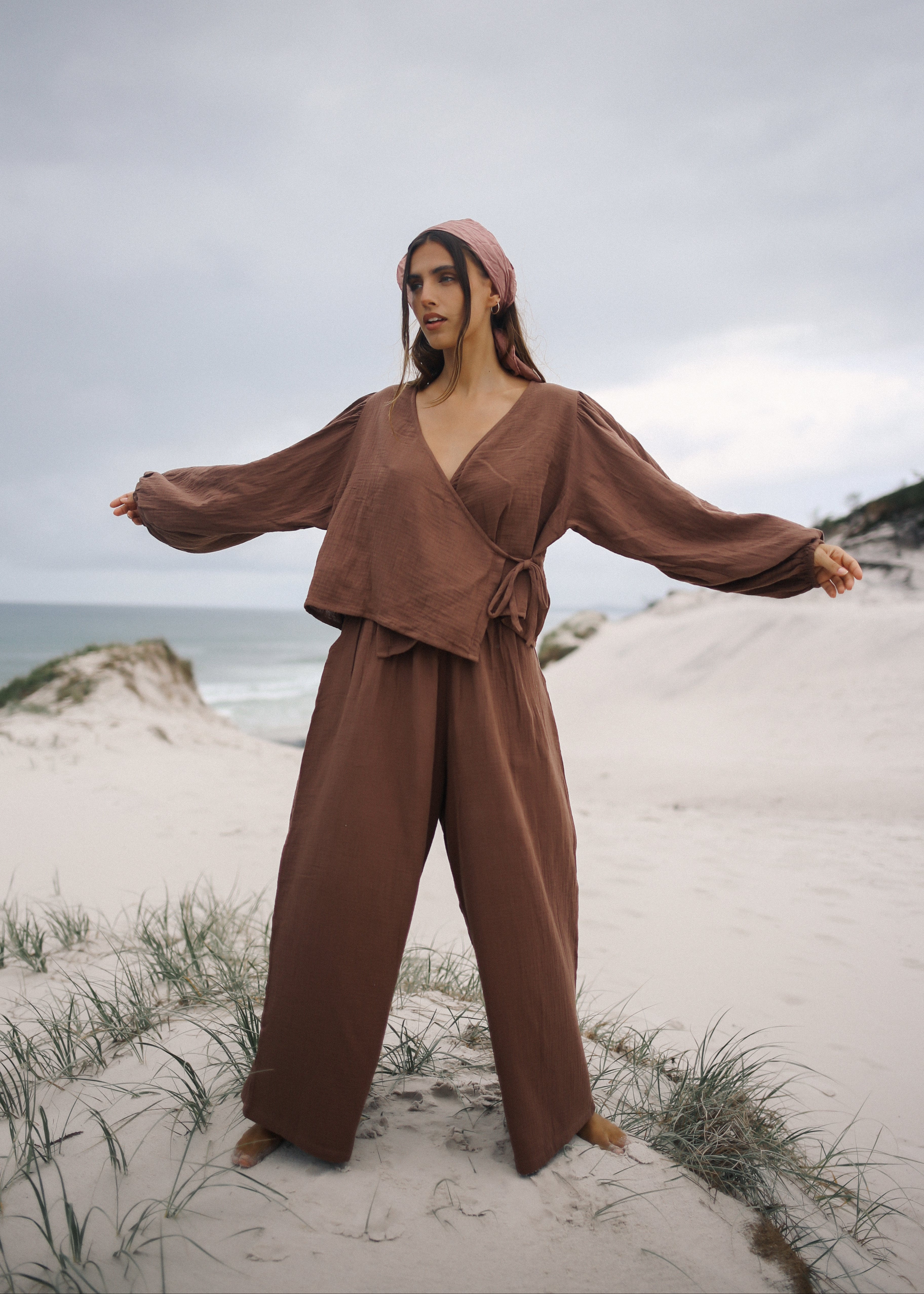 Woman in a brown outfit standing on a sandy beach with ocean and sky in the background