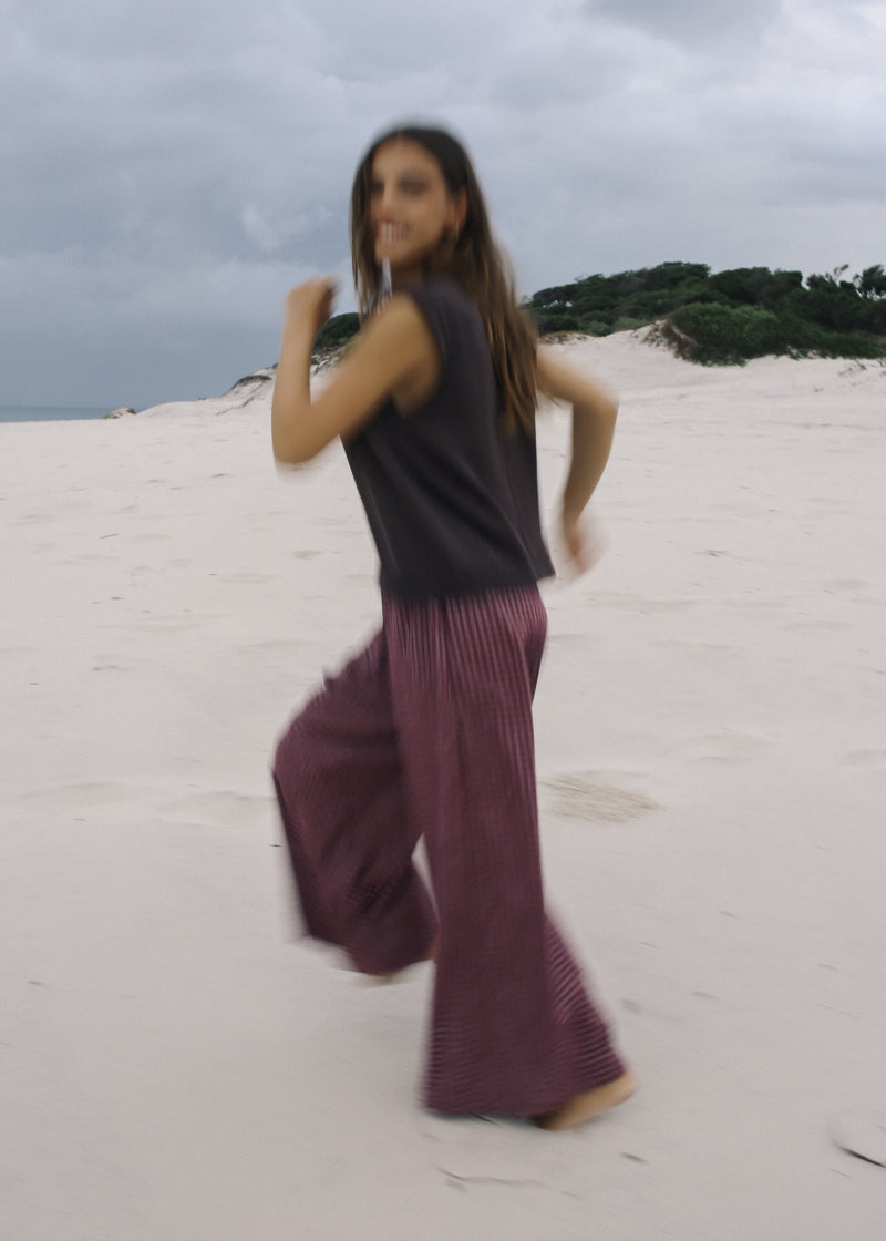 Woman in a black top and purple pants standing on a sandy dune with a cloudy sky.