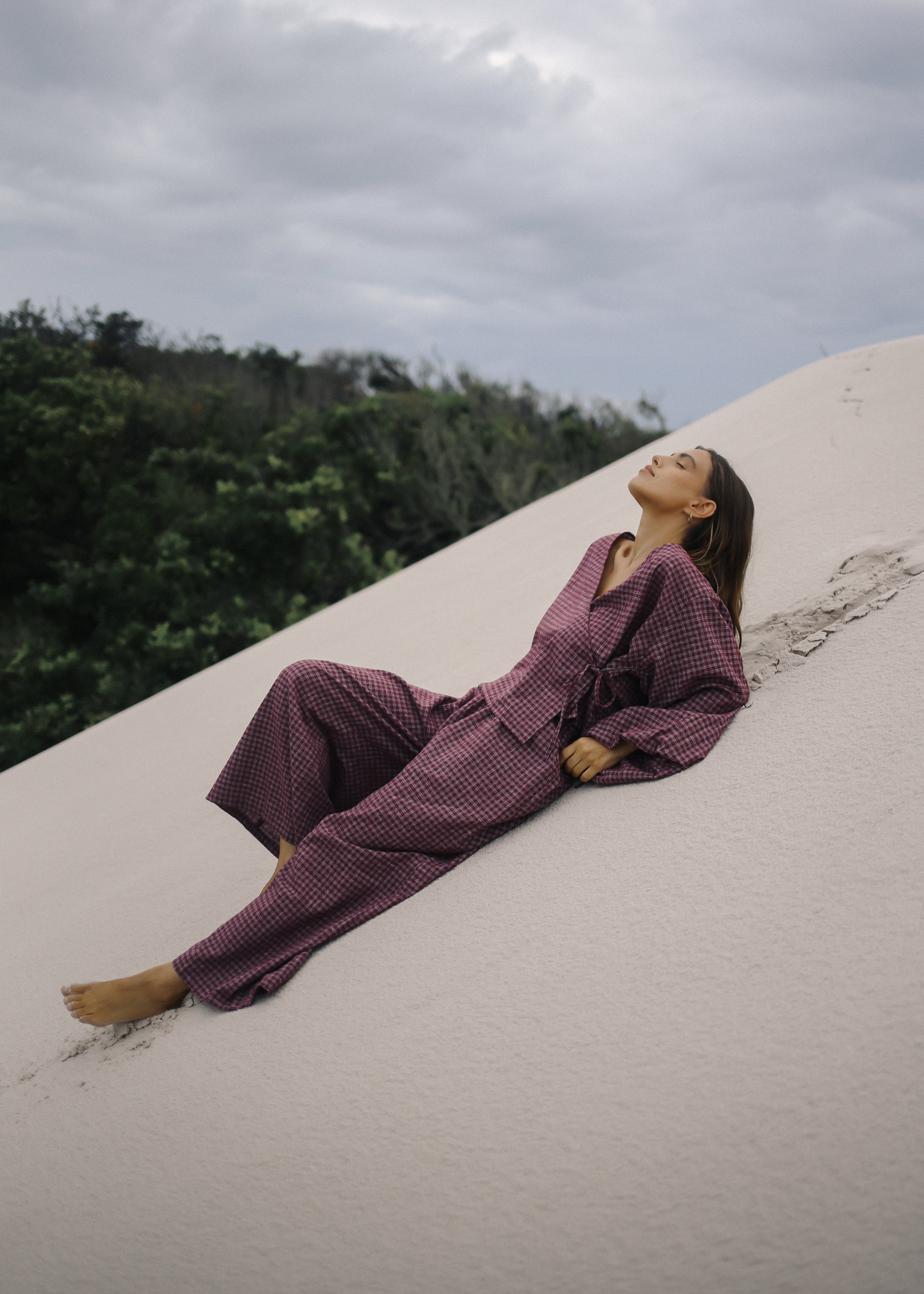 Person in a purple outfit lying on a sandy surface with greenery in the background